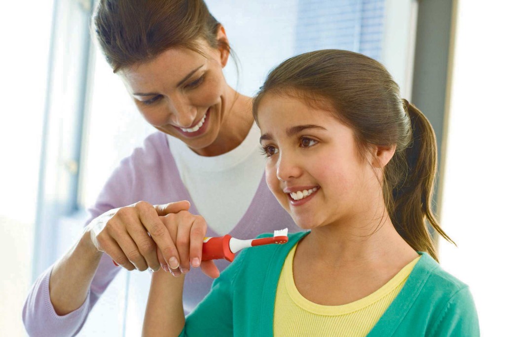 Girl brushing teeth with mum's help 