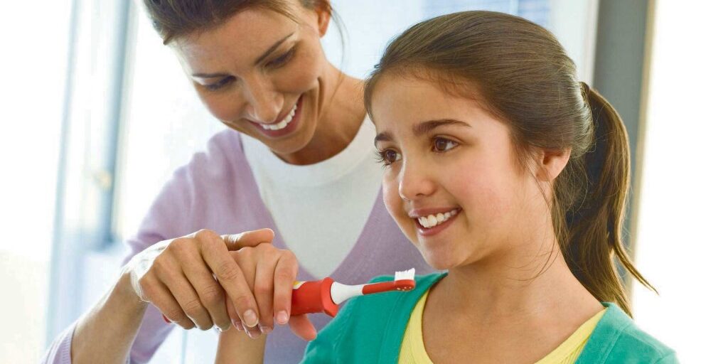 Girl brushing teeth with mum's help 